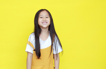 Portrait of happy asian little girl in dungarees with smiling isolated on yellow background with...