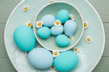 Plate with beautiful Easter eggs and flowers on wooden background