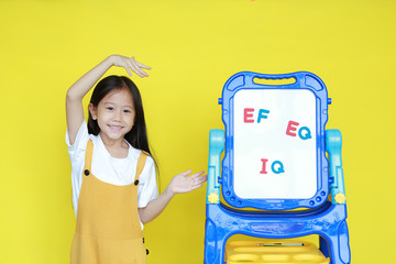 Asian little child girl present something on white board for study in class. Schoolgirl present text EF, EQ and IQ on whiteboard on yellow background. Student with brain development concept