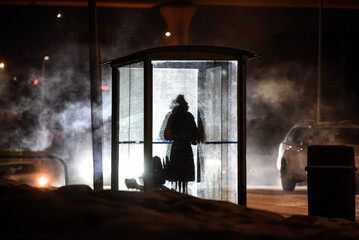Unidentified woman silhouetted at bus stop on foggy and cold morning