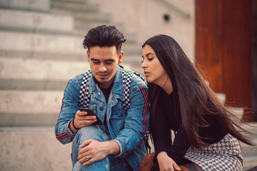 Portrait of young couple sit on a park bench and look at photos on a smartphone