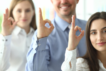 Focus on businesspeople demonstrating ok symbol. Smiling colleagues posing at modern office and looking at camera with gladness. Friendly teamwork concept