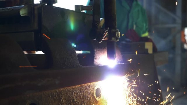 Plasma Cutter cutting through thick piece of steel with operator in the background. (Slow motion)