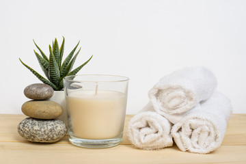 Fototapeta na wymiar Spa, relaxation and relaxation. Candle, towel, stones and a flower on a wooden and white background.