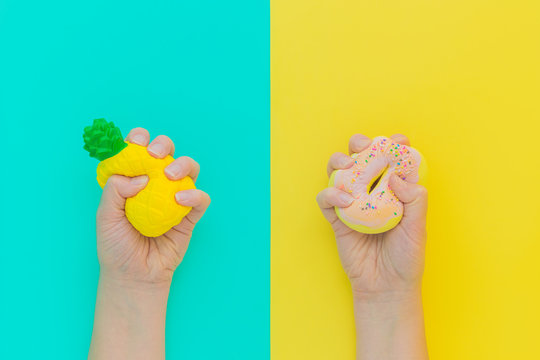 Flat lay antistress squish toys yellow pineapple,pink donut with sprinkles in hands.Bright blue background.Compressing,soft,squeezable items to relieve stress,problem,anxieties,worries.Summer concept