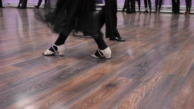 A couple dancing classic dance on the parquet floor. Legs of a young man and woman in a dance against a background of parquet floor. Close up 