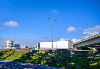 Obraz premium Big rig white day cab semi truck transporting goods in dry van semi trailer running on the highway entrance intersection
