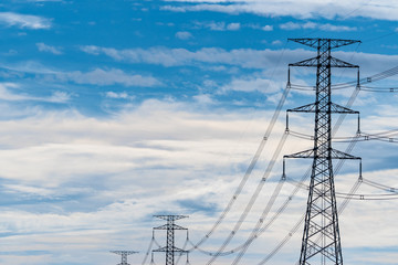 High voltage electric pole and transmission line. Electricity pylons. Power and energy. Energy conservation. High voltage grid tower with wire cable at distribution station against blue sky and cloud.