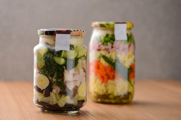 Homemade healthy russian salad Olivier with vegetables, meat and mayonnaise in glass jar on wooden table background