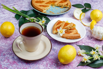 Delicious lemon pie slices with fresh lemons and a cup of tea on light background,top view