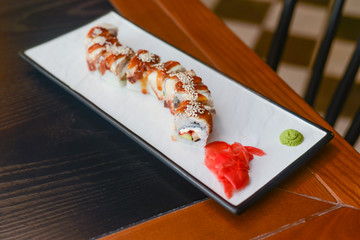 Salmon sushi rolls served on a white plate in a restaurant on wooden table. Japanese cuisine.