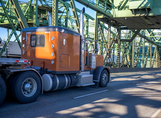 Classic commercial transportation brown big rig semi truck transporting cargo on flat bed semi trailer running on the truss Interstate Drawbridge