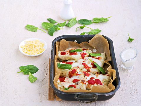 Crepes with spinach and ricotta cheese, baked with bechamel sauce and tomato sauce in a baking dish on a light concrete background. Easter Italian food. Italian food.
