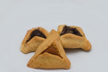 Hamantaschen. (ozen haman). Jewish food for Purim. Triangular crispy dough, stuffed with dates, halva and chocolate, on a white plate.