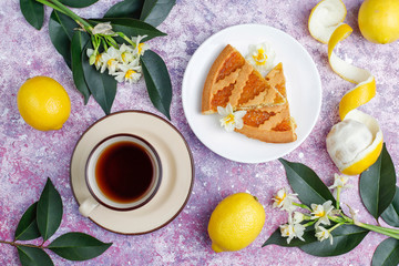 Delicious lemon pie slices with fresh lemons and a cup of tea on light background,top view