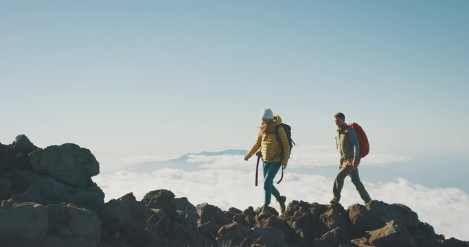 Young adventurous backpackers hiking to the top of a mountain above the clouds, happy couple hiking together in the great outdoors, amazing trekking on a mountain ridge