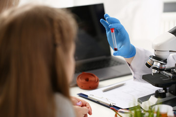Male hand in blue protective gloves holding test tube with blood sample against background of...