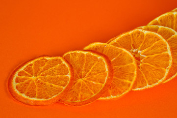 Chips of dried tangerines, sliced in thin circles. Shot on an orange background. Background for vegetarianism and healthy eating.