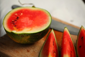 cutting fresh ripe watermelon into pieces with a knife on a wooden table