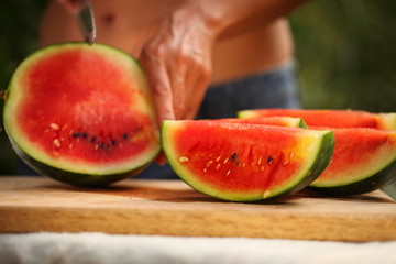 cutting fresh ripe watermelon into pieces with a knife on a wooden table