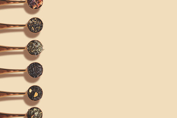 Spoons with assortment of tea on beige background with shadow
