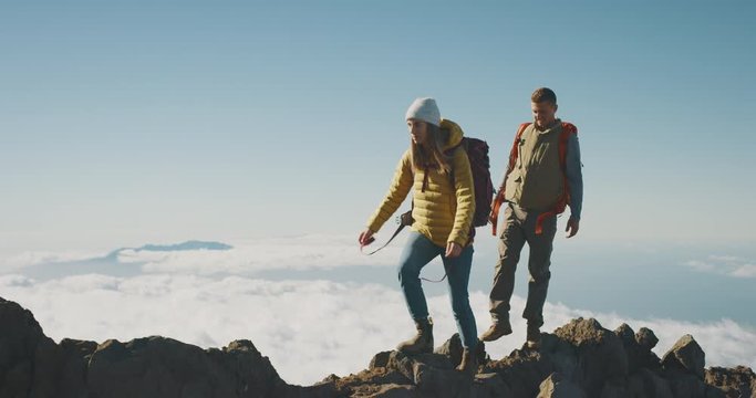 Young adventurous backpackers hiking to the top of a mountain above the clouds, happy couple hiking together in the great outdoors