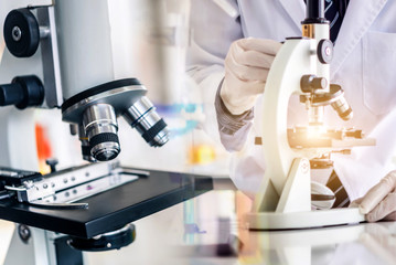 Scientist using microscope testing some blood sample at laboratory with lab glassware on the table. Science or medical research and development new antivirus concept.