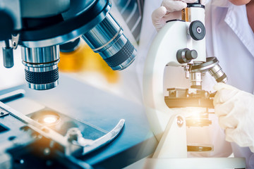 Scientist using microscope testing some blood sample at laboratory with lab glassware on the table. Science or medical research and development new antivirus concept.