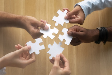 Hands of diverse team members assembling jigsaw puzzle close up