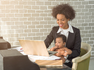 Young African mother with afro hairstyle working on labtop. Portrait of a happy mother with baby boy sitting on the lap while doing the job.