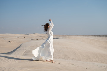 Brunette woman posing in windy desert in white light wedding dress