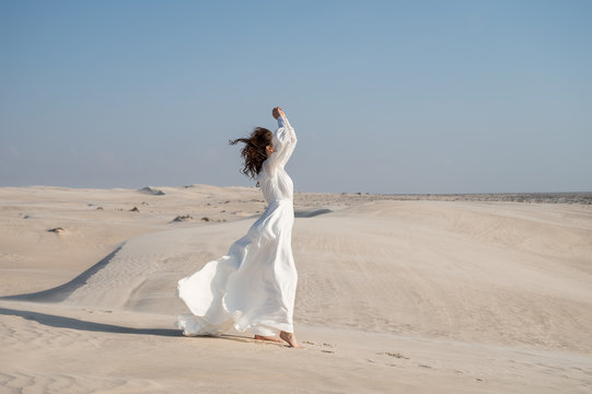 Brunette woman posing in windy desert in white light wedding dress