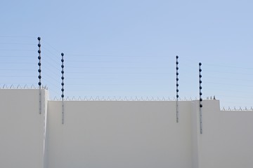 long upright poles holding electric fencing cable on a boundary wall