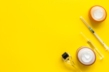Dermatologist work desk with tools. Dermaroller, syringe, ampoule on yellow background top-down flat lay copy space
