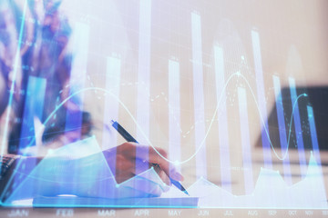 A woman hands writing information about stock market in notepad. Forex chart holograms in front....
