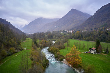 Alpine valley with mountain river and village cantoira with a lot of green  grass in a foggy autumn day 