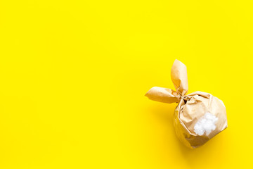 Easter gift in shape of bunny with tail on yellow background top-down copy space