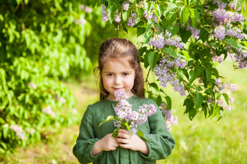 Cute girl has fun in the park with blooming lilacs, enjoys spring and warmth