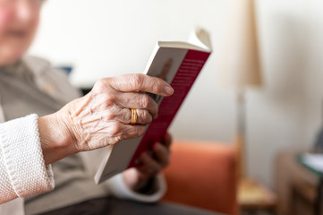 Old woman reading a book. Her wrinkled hand with her wedding ring and that of her deceased husband is close up.