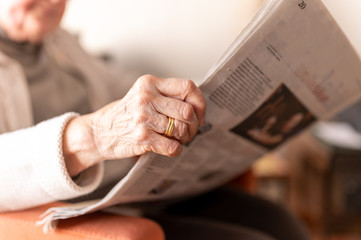 Obraz premium Old woman reading a newspaper. Her wrinkled hand with her wedding ring and that of her deceased husband is close up.