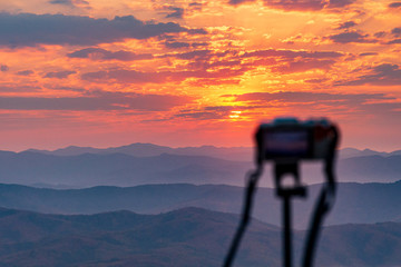 camera on tripod with sunrise above moutain background.