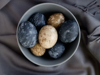 Easter background with Easter eggs and feathers in a ceramic gray bowl. Background with easter eggs. Naturally dyed eggs prepared for Easter on gray texture tablecloth background. Happy Easter