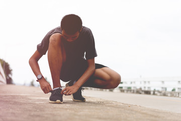 Tie a shoe,Asian male jogger athlete training and doing workout outdoors on a street, He tying laces for jogging on road with running shoes. Runner getting ready for exercise. Sport lifestyle concept