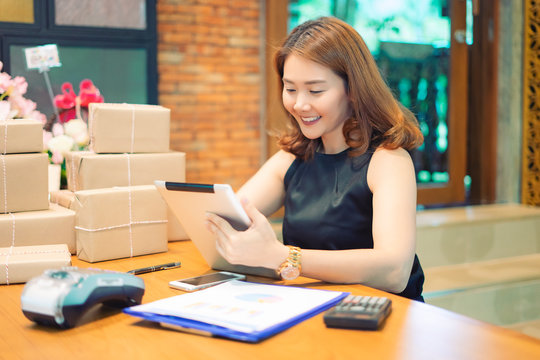 Asian woman using smartphone or digital tablets chatting and checking stock product in warehouse. checks the number of items boxes store delivery to customers, Asian owner or small business concept.