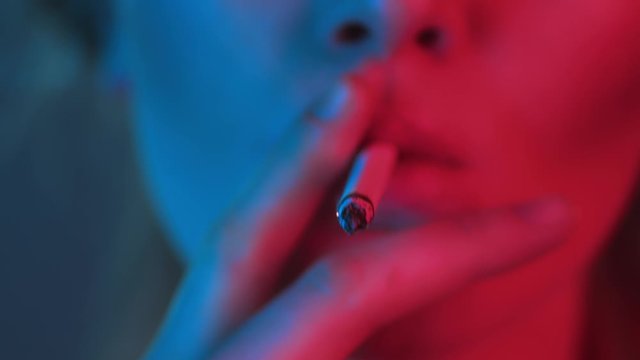 young girl takes drag or puff on cigarette in neon lighting, ember lights up, macro closeup of deep tobaco pull in night club or party, Smoking kills concept