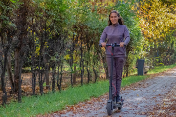 Obraz premium Woman is staying on electric scooter in autumn park. Active lifestyle. Modern ecologic transport. Modern city lifestyle.