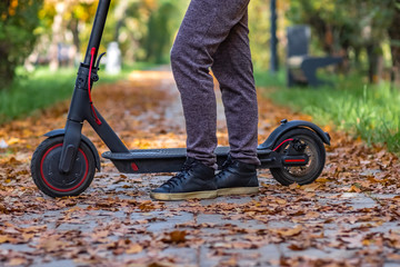 Obraz premium Woman is staying on electric scooter in autumn park. Active lifestyle. Modern ecologic transport. Modern city lifestyle.