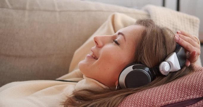 Happy woman listening songs using headphones while relaxing on sofa at home