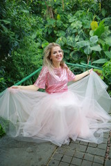 Fototapeta premium beautiful white long hair girl in a tropical garden in a light tulle pink skirt