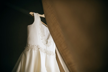 Wedding dress decoration. Beautiful white dress hanging on a hanger by the window. Bride morning